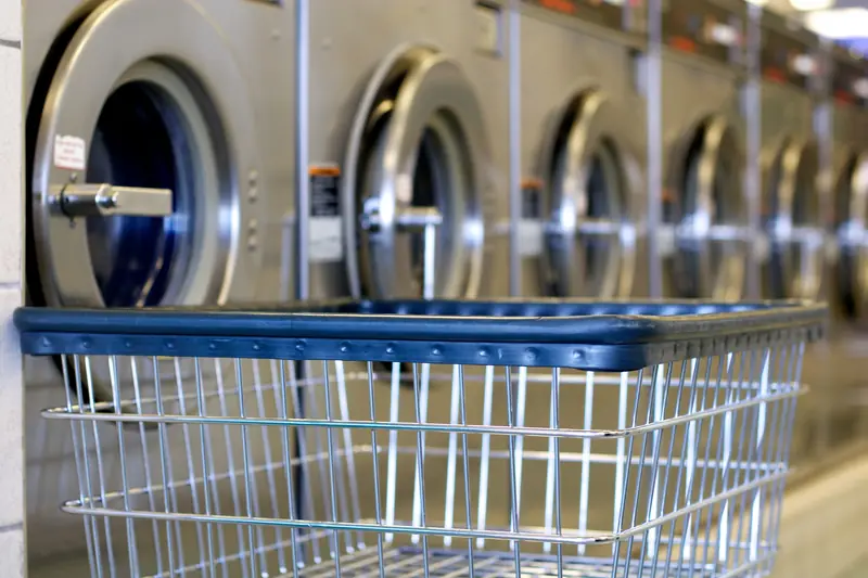 Row of stainless steel washers with a laundry cart in front